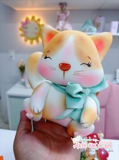 a hand holding a small toy cat in it's right hand, with other toys behind it