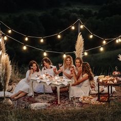 a group of women sitting around a table with food and drinks on it at night