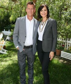 a man and woman standing next to each other in front of a tree on the grass