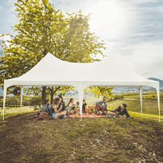 a group of people sitting under a white tent on top of a lush green field