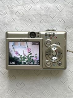 a camera is sitting on top of a white blanket with flowers in the front and side