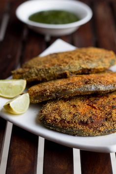 two fried fish on a white plate with lemon wedges and green pesto sauce