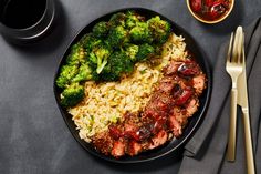 a plate with broccoli, meat and rice on it next to silverware