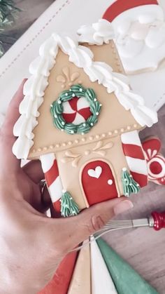 a hand holding a decorated gingerbread house with candy canes and wreaths on it