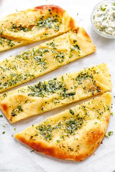 four slices of flat bread with herbs on top and a knife next to it, sitting on a piece of parchment paper