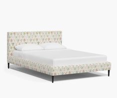 an upholstered bed with white linens and floral print on the headboard