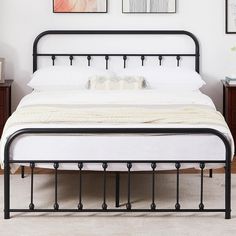 a white bed with black metal frame and headboard is in a room with pictures on the wall