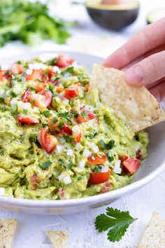 a person dipping guacamole into a bowl with tortilla chips on the side