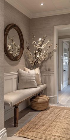 a white bench sitting next to a wooden table with flowers on it and a round mirror above it