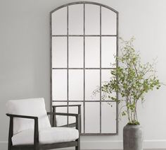 a white chair sitting in front of a large mirror on the wall next to a potted plant