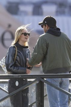 a man and woman standing next to each other on a balcony talking while holding hands