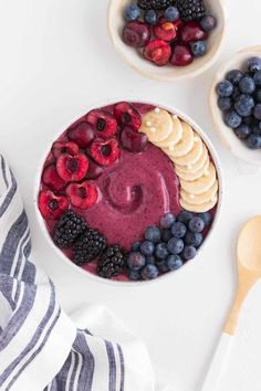 a bowl filled with berries and bananas next to two bowls of fruit on top of a white table