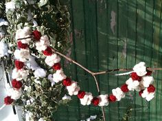 red and white flowers are hanging from a branch in front of a green door with snow on it