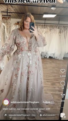 a woman taking a selfie with her phone in front of wedding gowns on display