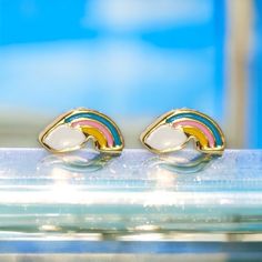 a pair of rainbow earrings sitting on top of a glass table in front of a blue wall