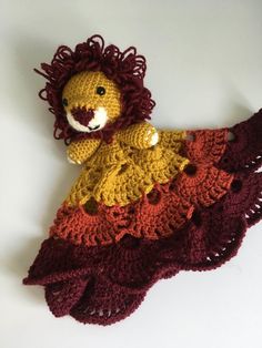 a crocheted stuffed lion is laying on the floor next to a red and yellow blanket