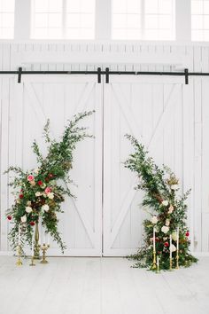 two white chairs with flowers and greenery on them in front of a barn door