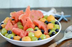 a white bowl filled with watermelon, grapes and blueberries on top of a wooden table