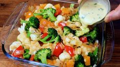 a person pouring dressing into a glass dish filled with vegetables and cauliflowers