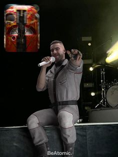 a man sitting on top of a stage holding a microphone in his right hand and singing into a microphone