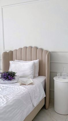 a bed with white sheets, pillows and a vase filled with flowers on top of it