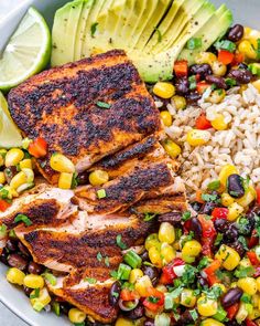 a bowl filled with chicken, rice and beans next to avocado wedges