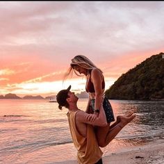 a man holding a woman on his back while they stand on the beach at sunset