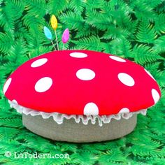 a red and white polka dot mushroom sitting on top of green grass with trees in the background