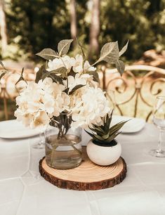 white flowers and greenery in vases on a wood slice at an outdoor table