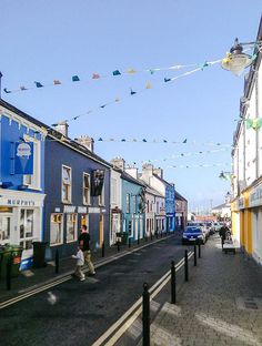 people walking down the street in front of colorful buildings with flags flying above them on a sunny day