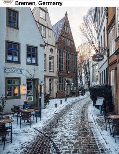 a cobblestone street with tables and chairs covered in snow next to tall buildings