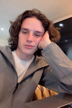 a young man sitting in front of a laptop computer with his hand on his head