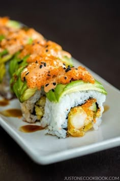 a white plate topped with sushi covered in sauce and garnished with avocado