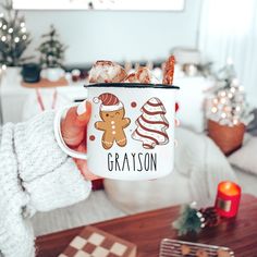 a person holding a coffee mug with some food in it and christmas decorations on the table