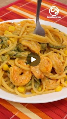 a white plate topped with pasta covered in shrimp and veggies next to a fork