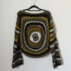 a crocheted sweater hanging on a hanger with an eyeball in the center