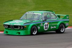 a green race car driving on a track with grass in the backgrouund