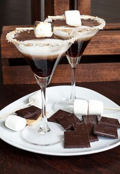 two glasses filled with chocolate and marshmallows on a white plate next to each other