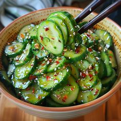 a bowl filled with sliced cucumbers and chopsticks in it on top of a wooden table