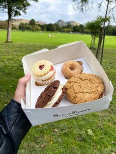 a person holding up a box filled with different types of donuts and cupcakes