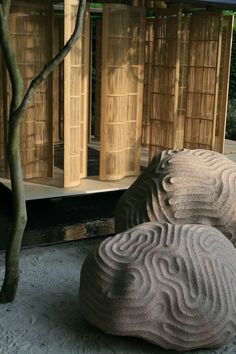 two large rocks sitting in front of a wooden structure with trees growing out of it