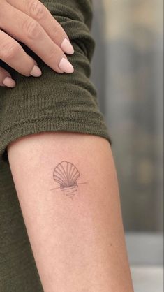 a woman's arm with a small shell tattoo on the left side of her leg