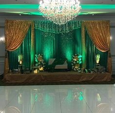 a green and gold stage set up with chandelier, curtains, and flowers