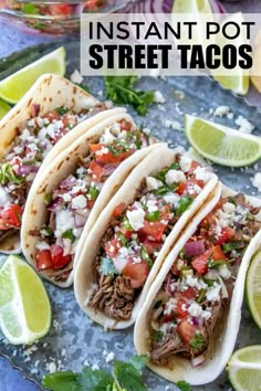 three tacos on a plate with limes, cilantro and red onion