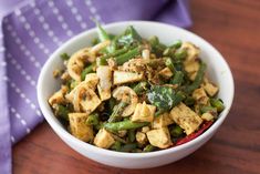 a bowl filled with green beans and tofu on top of a wooden table next to a purple napkin