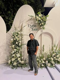 a man standing in front of a floral display at a fashion show with white flowers and greenery