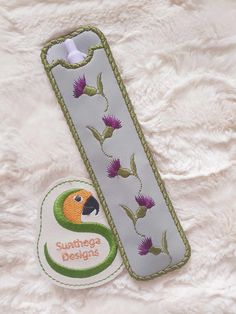 an embroidered bookmark with a bird and flower design on the front, sitting on a white furnishing