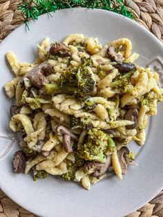 a white plate topped with pasta and broccoli covered in mushroom sauce on top of a woven place mat