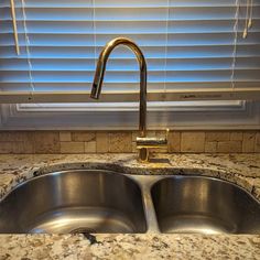 a kitchen sink with two faucets in front of a window covered by blinds