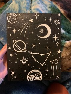 someone is holding up a black and white painting with stars, planets, and the moon